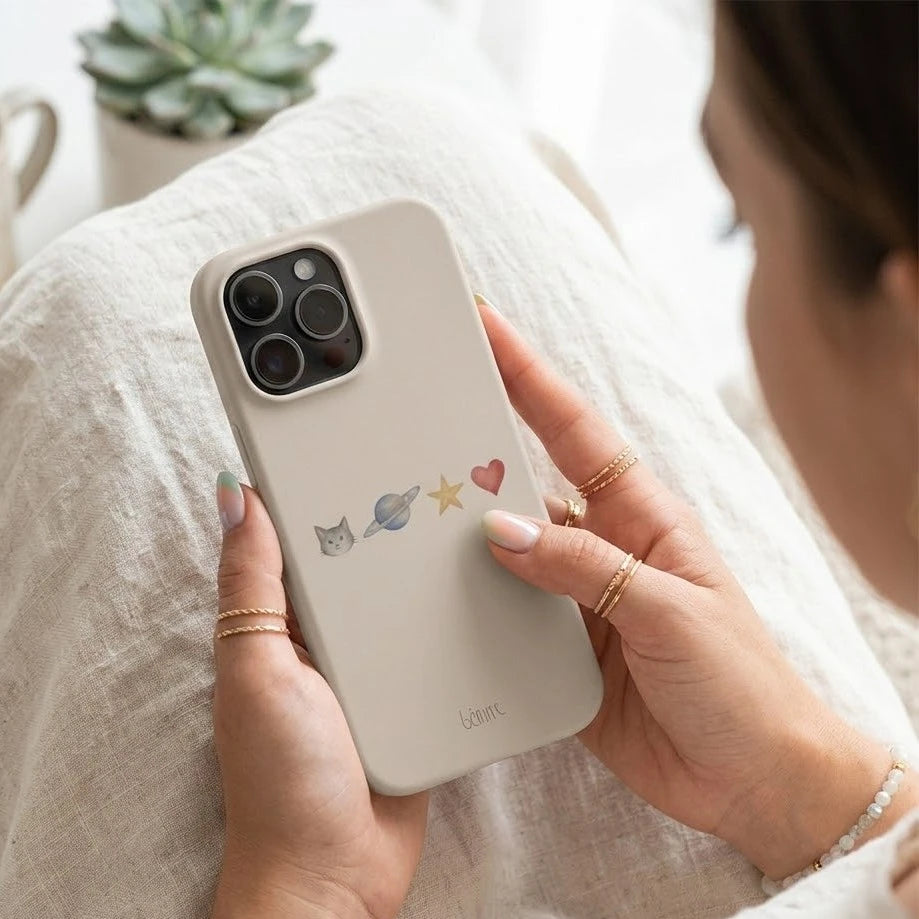 Person holding an iPhone with a beige case featuring cute cat illustrations.